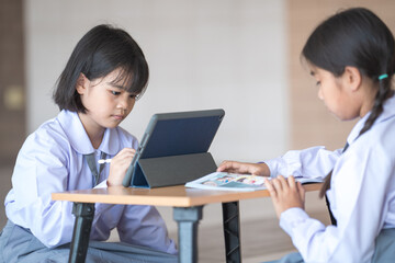 Asian children student friends back to school and study together using digital tablet and write on notebook at school afet Covid-19 lockdown. Back to School Concept Stock Photo