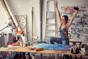 A young sexy and relaxed female artist is enjoying the music while painting in her studio. Art,...