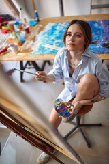 A young sexy and attractive female artist is sitting in front of the easel and brainstorming over...