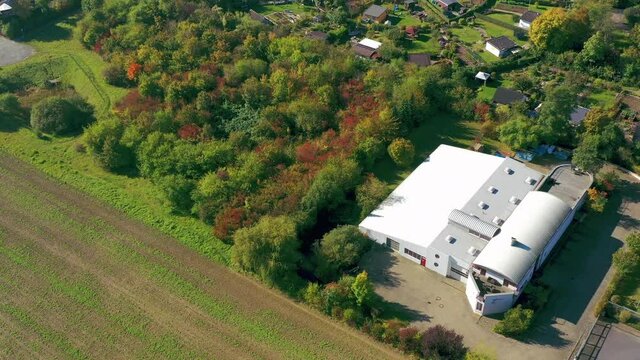 Aerial view during a reverse flight of a modern small warehouse on the edge of a field