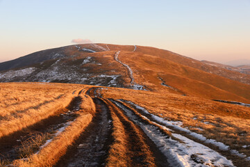 Autumn landscape in the Carpathian mountains. Dirt road with snow on the Borzhava ridge. Sunset lighting