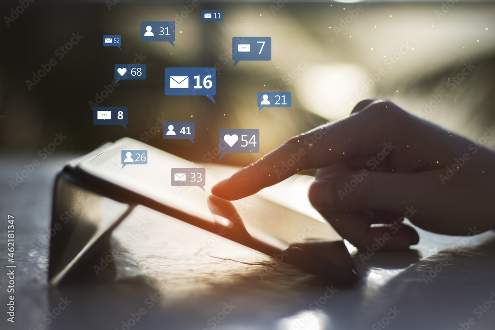 Poster close up of hand using tablet device at desktop with social media icons on blurry outdoor background