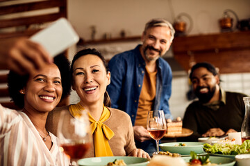 Happy multi-ethnic friends take selfie during lunch at dining table.
