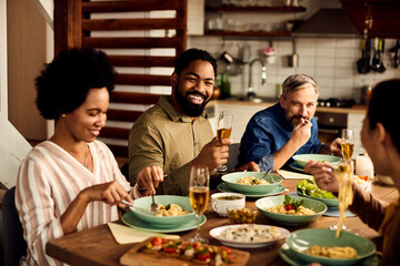 Happy multi-ethnic people have fun while drinking wine and talking during meal at dining table.