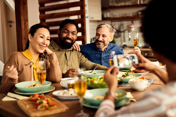 Group of happy multi-ethnic friends take picture while having lunch together at dining table.
