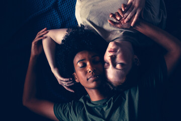 cute lesbian multiethnic couple in love lying down face to face and holding hands relaxing in room with morning sun