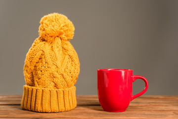 red cup of tea near knitted hat on wooden surface isolated on grey