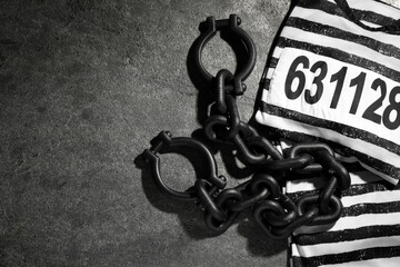 Steel shackles and jail clothes on grey table, flat lay. Space for text