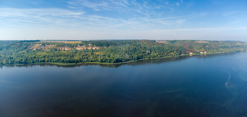 High river bank covered with forest, aerial view above water