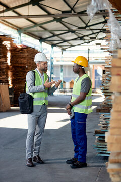 Full length of manager talks to African American worker lumber warehouse.