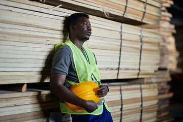 Young black warehouse worker feels tired while working at wood storage compartment.