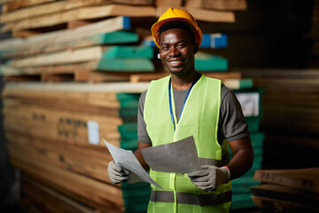 Happy black warehouse worker works at wood storage compartment and looks at camera.