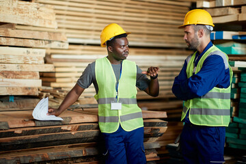 Two warehouse workers talk while working at lumber storage compartment.