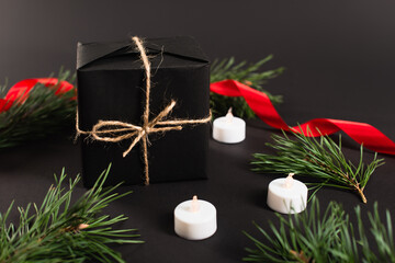 wrapped present near fir branches and candles with blurred red ribbon on black background