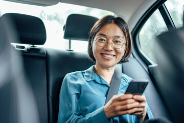 Mature businesswoman traveling by car, smiling at camera and using smart phone.