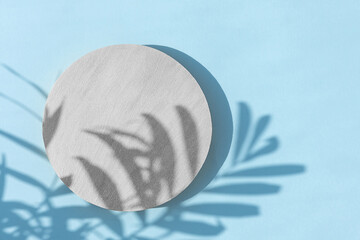 Abstract minimal scene of a geometrical form. A cylindrical silver podium on a blue background with a shadow of tropical palm leaves. Scene to show cosmetic podructs. Showcase, display case.