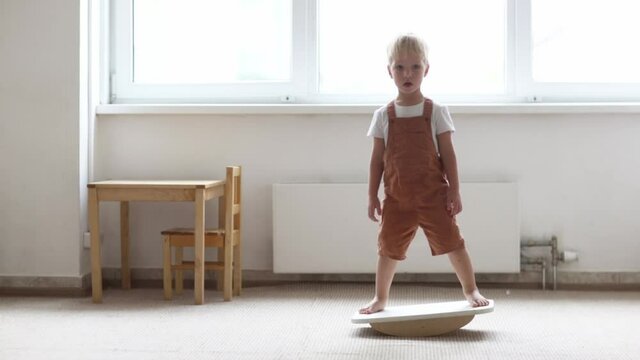 Cute toddler child boy swinging on a balancing board in a light room, physical and sensory development of children