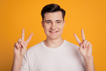 Portrait of young man showing two v-signs fingers against yellow background