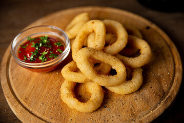 Onion rings with ketchup on a wooden board. Bar food. One serving. Sprinkled with ground pepper.