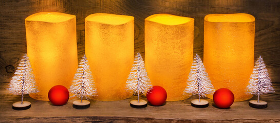 4 golden electric LED wax candles and Christmas decoration on wooden background