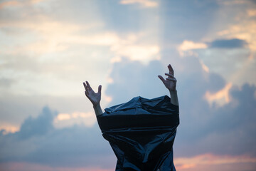 Women's hands out from a black plastic bag on a sunset sky background