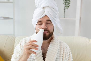 Bearded male with towel on his head applying body lotion cream. Guy smile when smell lotion cream on hand. Spa, body and skin care for man concept