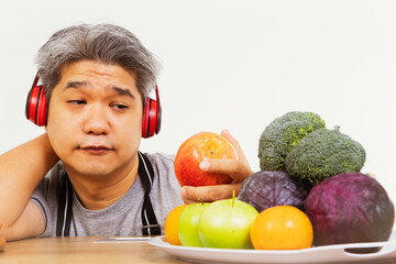Fototapeta premium Obese men look at fruits and vegetables, do not want to eat, are sitting and reviewing their diet to lose weight : He chooses to eat only apples.