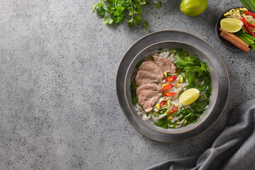 Pho Bo Soup with beef in gray bowl on gray background. View from above. Copy space. Vietnamese and Asian cuisine.