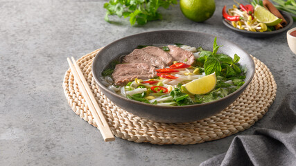 Pho Bo Soup with beef in gray bowl on gray stone background. Close up. Vietnamese and Asian cuisine.