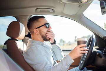 Young handsome man feeling tired and yawning while driving a car.