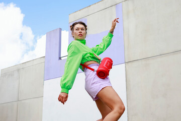 Young woman with speaker dancing by wall
