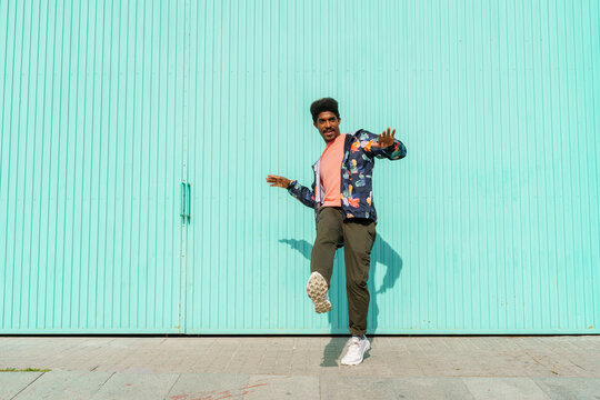 Man dancing in front of of turquoise wall during sunny day