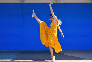 Carefree woman dancing by blue wall on sunny day