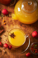 Glass teapot and cup with sea buckthorn tea with spices and autumn small crabapples on wooden background
