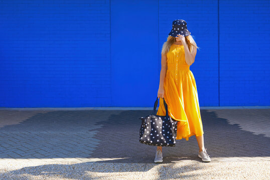 Mature woman with duffel bag and bucket hat in front of blue wall