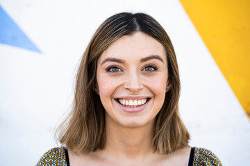 Woman with brown eyes smiling in front of wall
