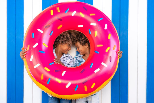 Smiling brothers standing face to face with inflatable doughnut