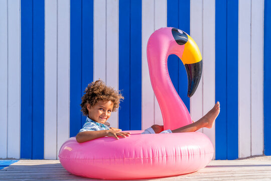 Cute curly haired boy sitting in inflatable flamingo