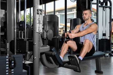 young man trains the muscles of the shoulder girdle and abdominal press using a cable weight machine in the gym
