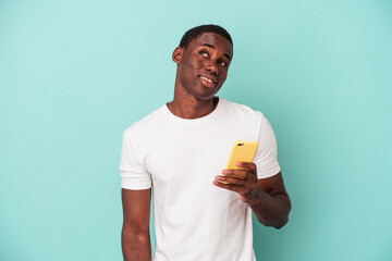 Young African American man holding a mobile phone isolated on blue background dreaming of achieving...