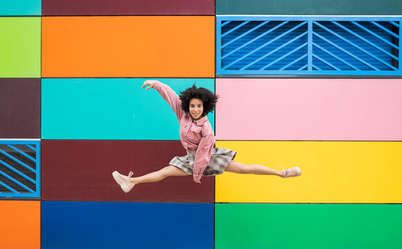 Female dancer jumping with leg splits in front of multi colored wall