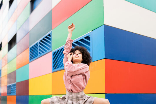 Female dancer with hand raised in front of colorful building