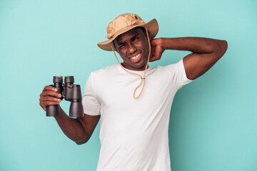 Young African American man holding binoculars isolated on blue background touching back of head, thinking and making a choice.