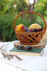 Vintage basket with various fruit, book, sunglasses and lavender flowers on a picnic basket. Selective focus.