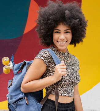 Smiling woman wearing Leopard print top while carrying backpack with skateboard