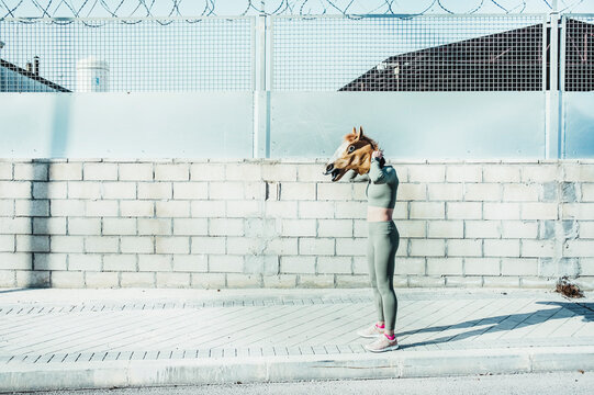 Mature Woman Wearing Horse Mask While Standing On Footpath