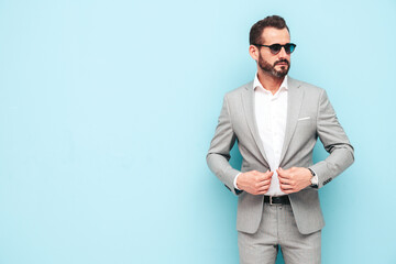 portrait of handsome confident stylish hipster lambersexual model.Sexy modern man dressed in elegant suit. Fashion male posing in studio near blue wall in sunglasses