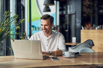 Smiling businessman working on laptop in cafe