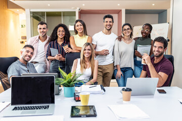 Successful business team posing around laptop for presentation of work while looking at camera in a...