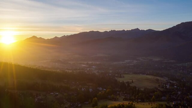 Aerial time lapse hyperlapse morning in highland village lit with warm sunlight. Drone shot sun rises over mountain range. Incredible view valley in sunrise light. Hilly area, clouds moving fast